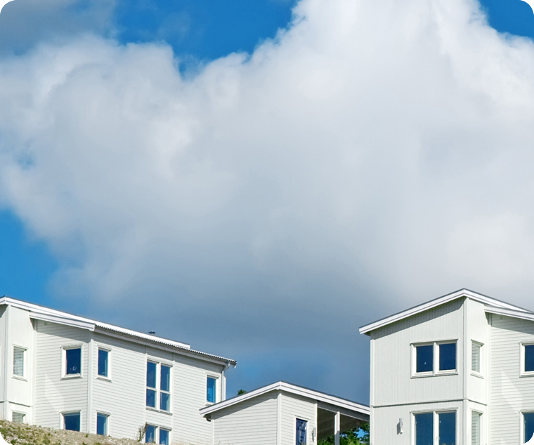 Nybyggda vita flerbostadshus mot en vacker blå himmel med moln