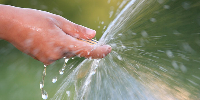 En hand håller i en vattenslang med pekfingret framför så vattnet sprids