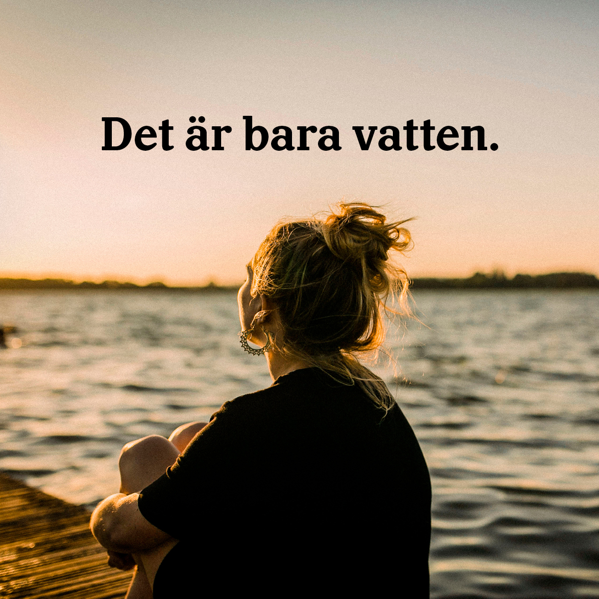 Person sitter och tittar ut över sjö med solnedgång